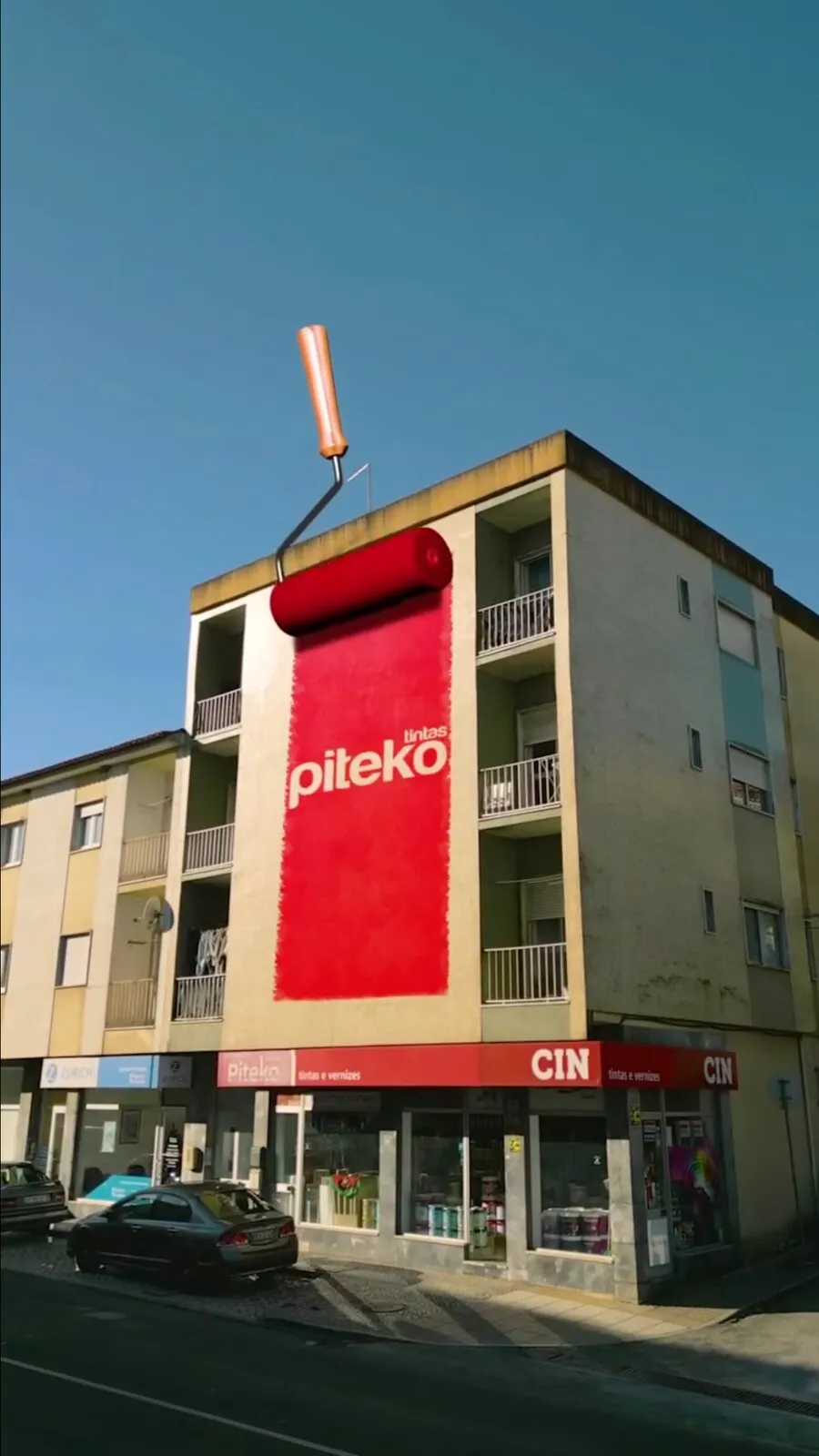 Piteko video frame: a giant 3D paint roller painting the building façade red with the brand